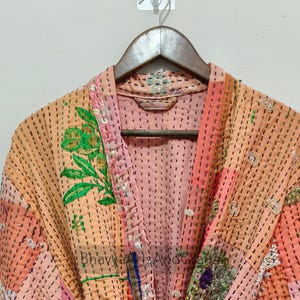 May include: A patchwork robe in shades of peach, pink, and orange, with embroidered floral details in green and gold. The robe has a tie closure and is made of quilted fabric. The text "Bhavya Arts And Goods" is visible on the robe.