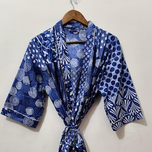 May include: A blue and white patterned robe hanging on a wooden hanger. The robe features a variety of designs, including circles, dots, and leaf-like shapes. The robe is tied at the waist with a matching fabric belt.
