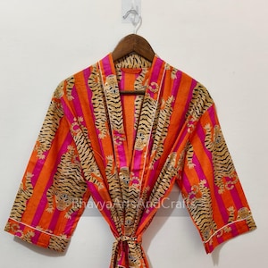May include: A vibrant orange and pink striped robe with a tiger print. The robe has a tie closure and white trim. The robe is hanging on a wooden hanger.
