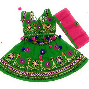 May include: A green embroidered dress with a matching pink scarf. The dress features floral and mirror embellishments, with a decorative waistline and neckline. The outfit is designed with a traditional aesthetic.