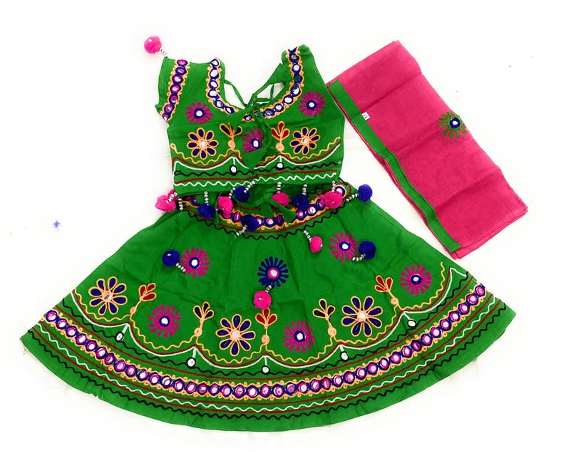 May include: A green embroidered dress with a matching pink scarf. The dress features floral and mirror embellishments, with a decorative waistline and neckline. The outfit is designed with a traditional aesthetic.