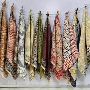 Könnte beinhalten: Eine Sammlung von zehn gemusterten Stoffschals, die an einer Schnur hängen. Die Schals zeigen eine Vielzahl von Farben, darunter Braun, Rot, Grün und Creme, mit aufwendigen Blockdruckmustern. Jeder Schal ist etwa 61 cm lang.