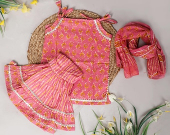 May include: A pink floral print outfit set, including a top with tie straps, a flared skirt, and a matching scarf. The set features white lace trim and yellow floral accents. The outfit is displayed on a woven mat with floral decorations.
