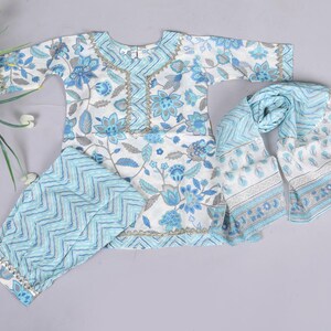 K&ouml;nnte beinhalten: Ein wei&szlig;-blaues Outfit mit Blumenmuster, bestehend aus einem Oberteil, einer Hose und einem Schal. Das Oberteil hat einen runden Ausschnitt und lange &Auml;rmel. Die Hose hat ein Zickzackmuster. Der Schal hat ein Blumen- und Paisley-Design.