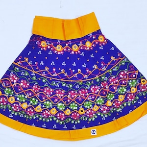 May include: A vibrant blue skirt with intricate embroidery and mirror work. The skirt features a bright yellow waistband and hem. The design includes floral and geometric patterns in shades of red, green, and orange. A colorful and festive garment.