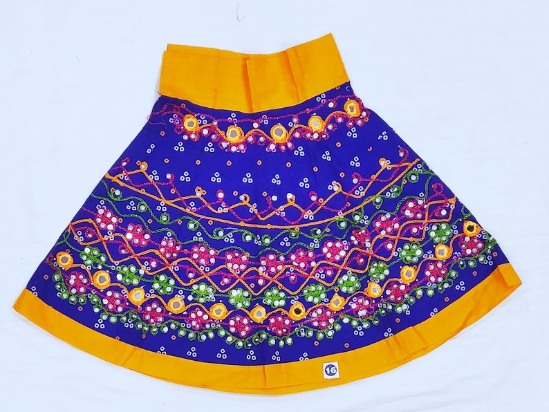 May include: A vibrant blue skirt with intricate embroidery and mirror work. The skirt features a bright yellow waistband and hem. The design includes floral and geometric patterns in shades of red, green, and orange. A colorful and festive garment.