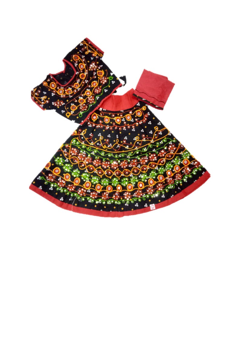 May include: A traditional Indian outfit featuring a black top and skirt, both adorned with colorful embroidery. The skirt has a red border, and a matching red scarf is included. The embroidery includes orange, green, and white floral patterns.