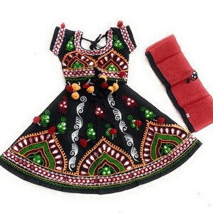 May include: Black embroidered dress with red, green, and white accents. The dress features a flared skirt and short sleeves, with a matching red scarf. The embroidery includes mirrors and pom-poms, creating a festive look.
