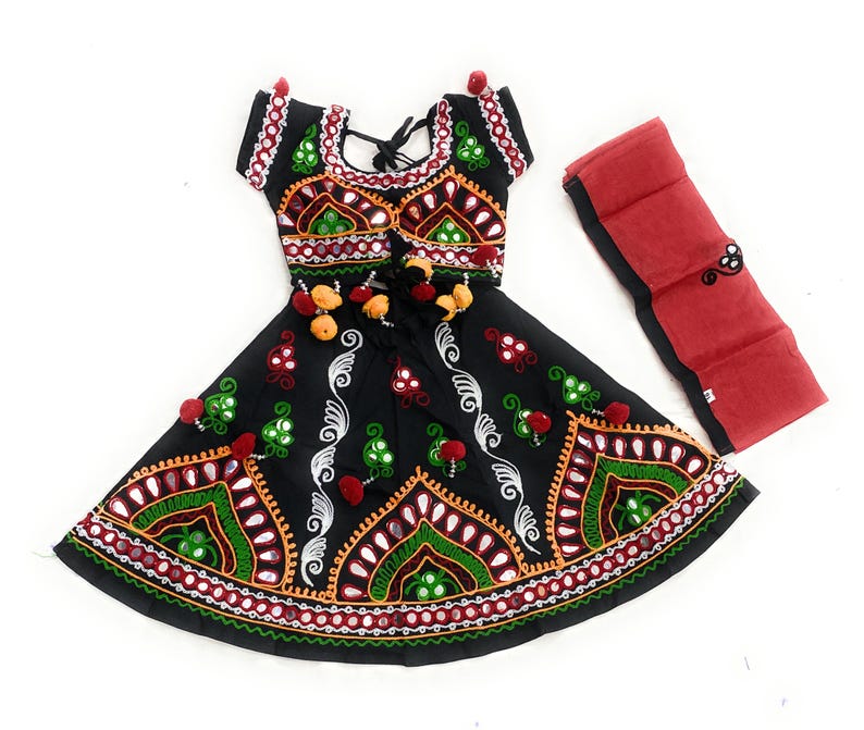May include: Black embroidered dress with red, green, and white accents. The dress features a flared skirt and short sleeves, with a matching red scarf. The embroidery includes mirrors and pom-poms, creating a festive look.