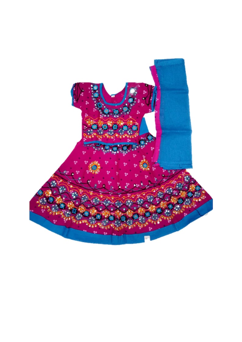 May include: A magenta-colored traditional Indian dress with intricate embroidery and mirror work. The dress features a short-sleeved top and a flared skirt, both adorned with blue and gold accents. A matching blue scarf is included.