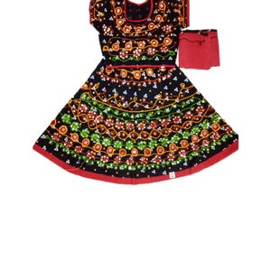 May include: Black dress with intricate embroidery in orange, green, and white. The dress features a red trim and a matching red accessory. The design includes floral and geometric patterns, creating a vibrant and detailed look. The dress is likely a traditional garment.