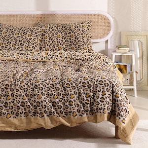 May include: A bed with a leopard print comforter and matching pillowcases. The bedding features a tan background with brown and yellow spots. The bed has a woven headboard and a striped border on the comforter.