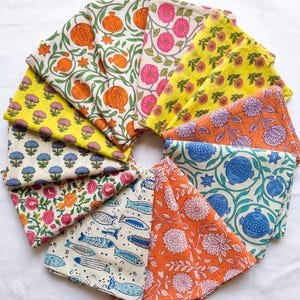 Puede incluir: Una colección de cuadrados de tela coloridos dispuestos en un patrón circular. Cada cuadrado presenta un estampado floral o botánico único en tonos naranja, rosa, azul y amarillo. Las telas son probablemente de algodón o lino, perfectas para manualidades o decoración del hogar.