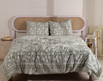 May include: A bed with a light green and white floral patterned quilt and two matching pillowcases. The headboard is a light pink color with a woven cane design. The bed is on a light-colored rug.