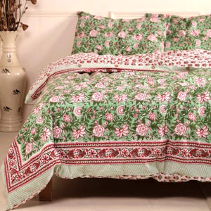 Pode incluir: Um conjunto de cama com padrão floral em verde e branco, com detalhes em vermelho. O conjunto inclui uma capa de edredão e fronhas, todas adornadas com um desenho floral repetido. A roupa de cama é feita de um material macio e confortável.