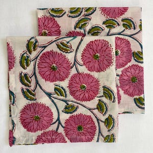 Op de afbeelding: Twee witte stoffen servetten met een herhalend bloemenpatroon. Het ontwerp toont grote roze bloemen, groene bladeren en turquoise ranken. De servetten zijn gevouwen en naast elkaar geplaatst, waardoor het volledige patroon wordt getoond.