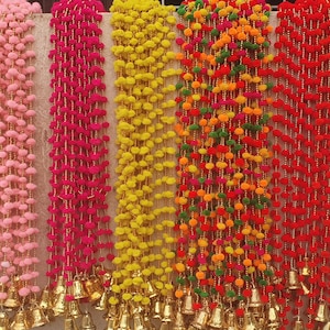 Puede incluir: Una colección de guirnaldas decorativas coloridas. Las guirnaldas están hechas de pequeños elementos redondos, tipo pompones, en tonos rosa, fucsia, amarillo, naranja, verde y rojo. Cada hebra está adornada con pequeñas campanas doradas en la parte inferior.