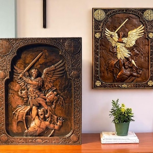 May include: Two wooden relief carvings. One shows a winged figure with a sword, battling figures below. The carvings are framed in ornate, dark brown wood. One is on a table, the other is hanging on a wall.