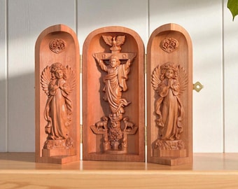 May include: A wooden triptych featuring carved religious figures. The central panel depicts a figure on a cross, flanked by panels with angel figures. The wood has a warm, reddish-brown tone, and the carvings are detailed.