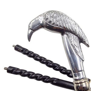 May include: A silver-colored walking cane with a bird-shaped handle. The handle is detailed with feather patterns. The black wooden shaft has a twisted design. The cane is a decorative accessory.