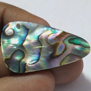 Könnte beinhalten: Schillernde Abalone-Schale mit einer einzigartigen, organischen Form. Die Schale zeigt ein faszinierendes Farbspiel, darunter Blau-, Grün-, Violett- und Goldtöne. Die Oberfläche hat ein glattes, poliertes Aussehen und zeigt die natürlichen Muster und Texturen.