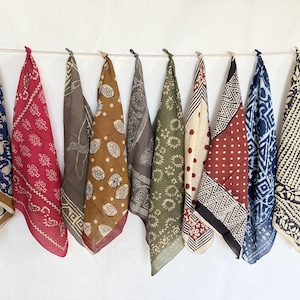 May include: Ten patterned bandanas in a variety of colours, including red, blue, brown, and green, suspended from a white string. Each bandana displays unique designs, such as paisley, dots, and geometric patterns.