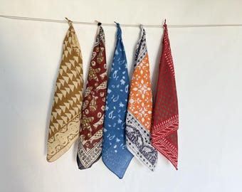 Peut inclure: Cinq bandanas à motifs suspendus contre un mur blanc. Les bandanas sont dans des tons de beige, bordeaux, bleu, orange et rouge. Chaque bandana a un design unique, comprenant des formes géométriques, des motifs cachemire et floraux. Les bandanas sont noués en haut.