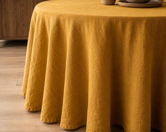 Op de afbeelding: Een rond mosterdgeel tafelkleed met een zichtbare geweven textuur gedrapeerd over een ronde tafel. De stof valt in zachte, verticale plooien rond de randen, waardoor een gelijkmatige plooi ontstaat die de zijkanten van het tafeloppervlak bedekt.