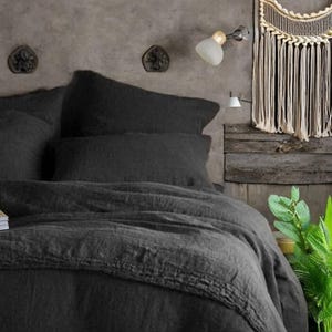 Könnte beinhalten: Ein dunkelgraues Bettwäsche-Set mit Kissen und einem Bettbezug. Die Bettwäsche besteht aus einem strukturierten Stoff. Die Szene umfasst einen Makramee-Wandbehang, eine kleine Lampe und dekorative Wandakzente.