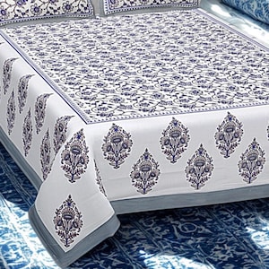 Può includere: Set di lenzuola bianche con motivo floreale blu. Il lenzuolo presenta un motivo ripetuto di fiori e foglie stilizzati, con un bordo di motivi simili. L'estetica generale è pulita ed elegante, adatta per una camera da letto.