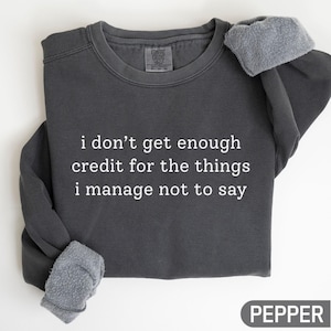 May include: A dark gray sweatshirt with the text "i don't get enough credit for the things i manage not to say" in white. The sweatshirt has a fleece lining and the word "PEPPER" is in a box at the bottom.
