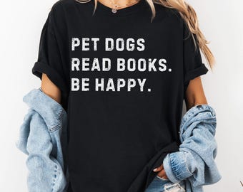 May include: Black t-shirt with the text "PET DOGS READ BOOKS. BE HAPPY." in white block letters. The shirt is a crew neck style and is being worn by a person. The word "BLACK" is printed in white in the bottom right corner.