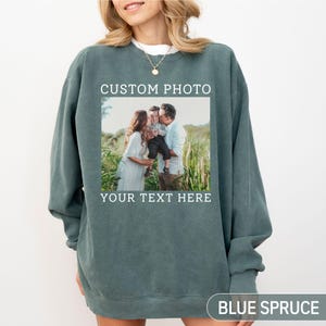 May include: Blue spruce-colored sweatshirt with a custom photo and text. The photo shows a family of three. The text on the sweatshirt reads "CUSTOM PHOTO" above the photo and "YOUR TEXT HERE" below it. The words "BLUE SPRUCE" are at the bottom.
