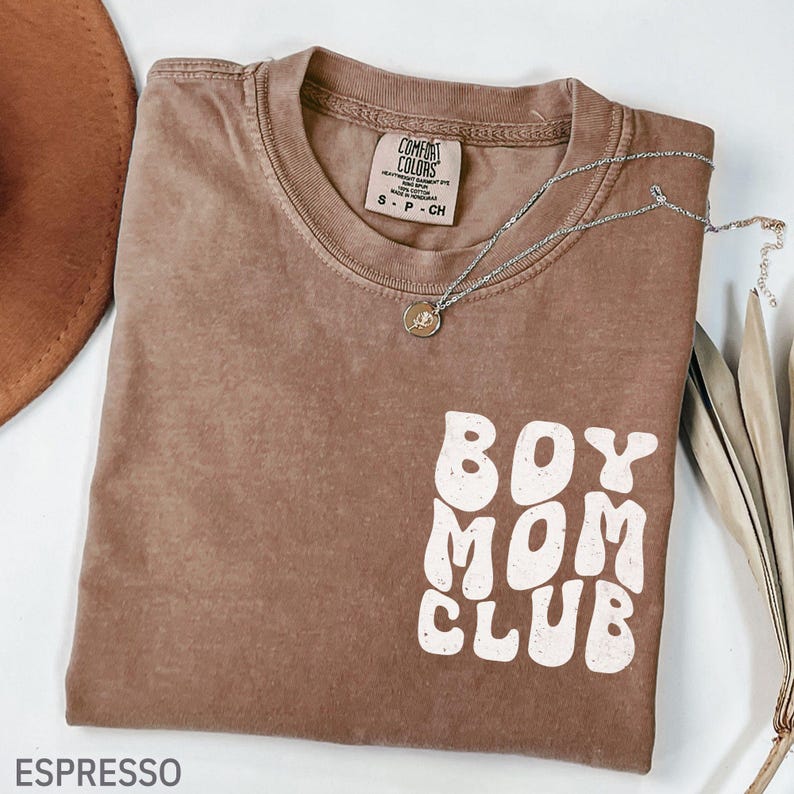 以下が含まれることがあります： エスプレッソ色のTシャツ。白で「BOY MOM CLUB」の文字、シルバーのネックレス、茶色の帽子。シャツはComfort Colorsブランド、サイズS-P-CHです。