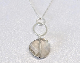 May include: A silver necklace featuring a delicate chain connected to a circular silver ring, which suspends a single, faceted, translucent, light brown, round gemstone pendant with a vertical silver bar detail running through the center.