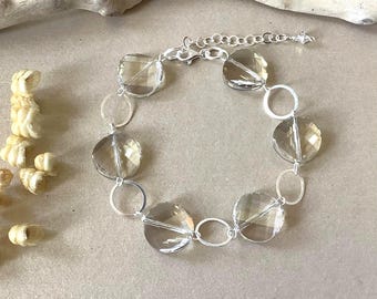 May include: A bracelet featuring four faceted, translucent, light brown circular stones alternating with four polished silver-tone metal rings. The piece includes a silver-tone chain with a lobster claw clasp and an adjustable extender link.