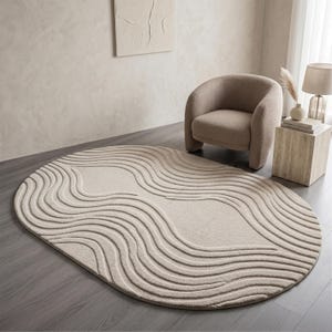 May include: An oval-shaped beige rug with a wave-like pattern. The rug is made of a soft material and has a textured surface. The rug is placed on a dark gray wooden floor. The rug is a decorative item for a living room or bedroom.