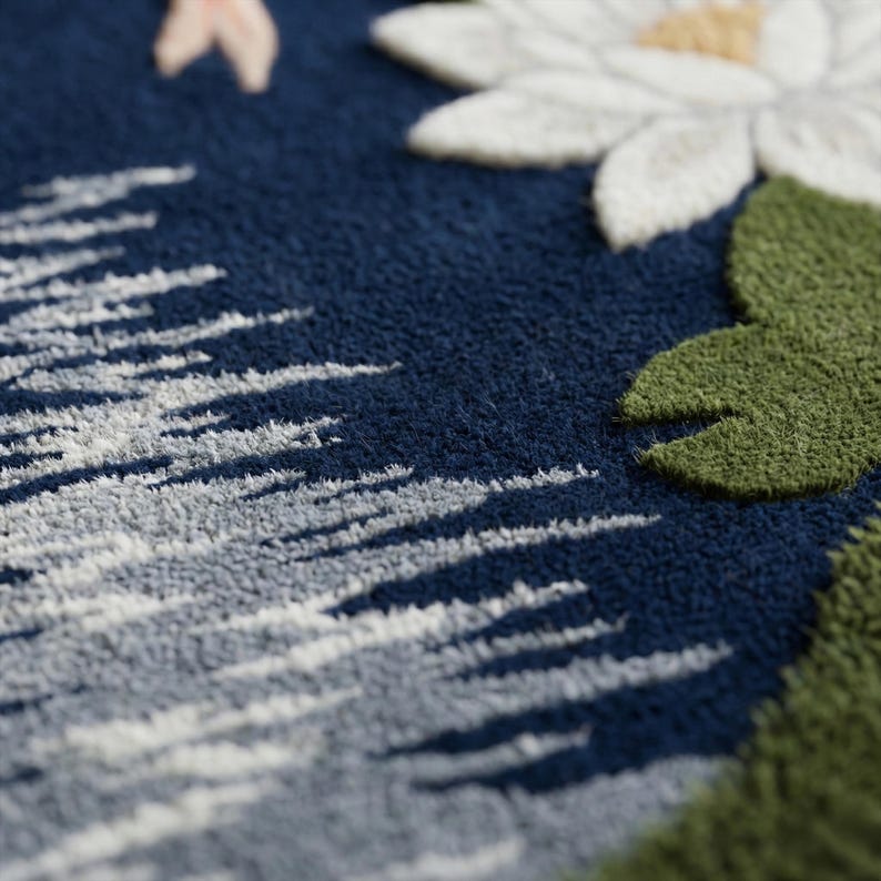 May include: Close-up of a navy blue textile with embroidered white and gray abstract shapes, a white flower with a yellow center, and green leaves. The texture appears soft and plush, suggesting a rug or decorative item.