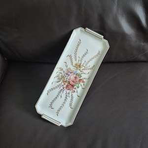 May include: A rectangular, off-white serving tray with a floral bouquet design in the center. The bouquet features pink, red, yellow, and blue flowers. Gold accents frame the tray and adorn the sides.