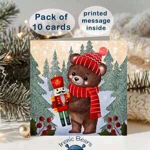 May include: Christmas greeting cards featuring a brown bear wearing a red hat and scarf, holding a nutcracker. The card has a snowy forest scene with the text "Pack of 10 cards" and "printed message inside".