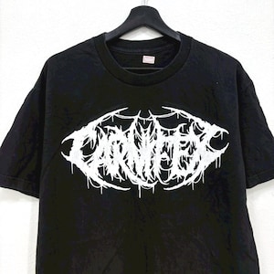 May include: Black t-shirt with a white, stylized graphic design. The design features the word "CARNIFEX" in a dripping, gothic font. The shirt is hanging on a black hanger.