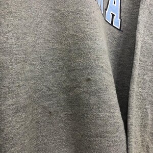 May include: A gray sweatshirt with the word "CAROLINA" in light blue block letters across the top. The letters have a white outline. The fabric appears to be a soft, textured material.