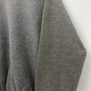 May include: Close-up of a gray sweatshirt. The fabric appears to be a soft, textured material. The image focuses on the sleeve and part of the body of the garment. The sweatshirt is a solid, medium gray color.