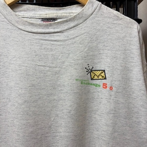 Könnte beinhalten: Ein hellgraues, meliertes T-Shirt mit Rundhalsausschnitt und einer kleinen Grafik auf der Brust. Die Grafik zeigt ein gelb-schwarzes, verpixeltes Briefumschlag-Symbol mit dem Text Microsoft Exchange 5.0 in Grün und Rot. Das Shirt hat ein Oneita Power Etikett.