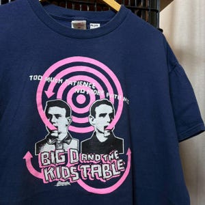 May include: Navy blue t-shirt featuring a pink graphic with the text "TOO MUCH PATIENCE NO MORE PATIENCE" and "BIG D AND THE KIDSTABLE". The graphic includes two black and white portraits. A vintage tee.