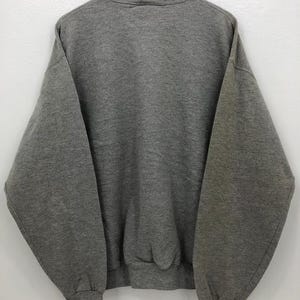 May include: A heather gray sweatshirt with a crew neck and long sleeves. The sweatshirt is hanging on a wooden hanger against a white background. The cuffs and hem are ribbed.