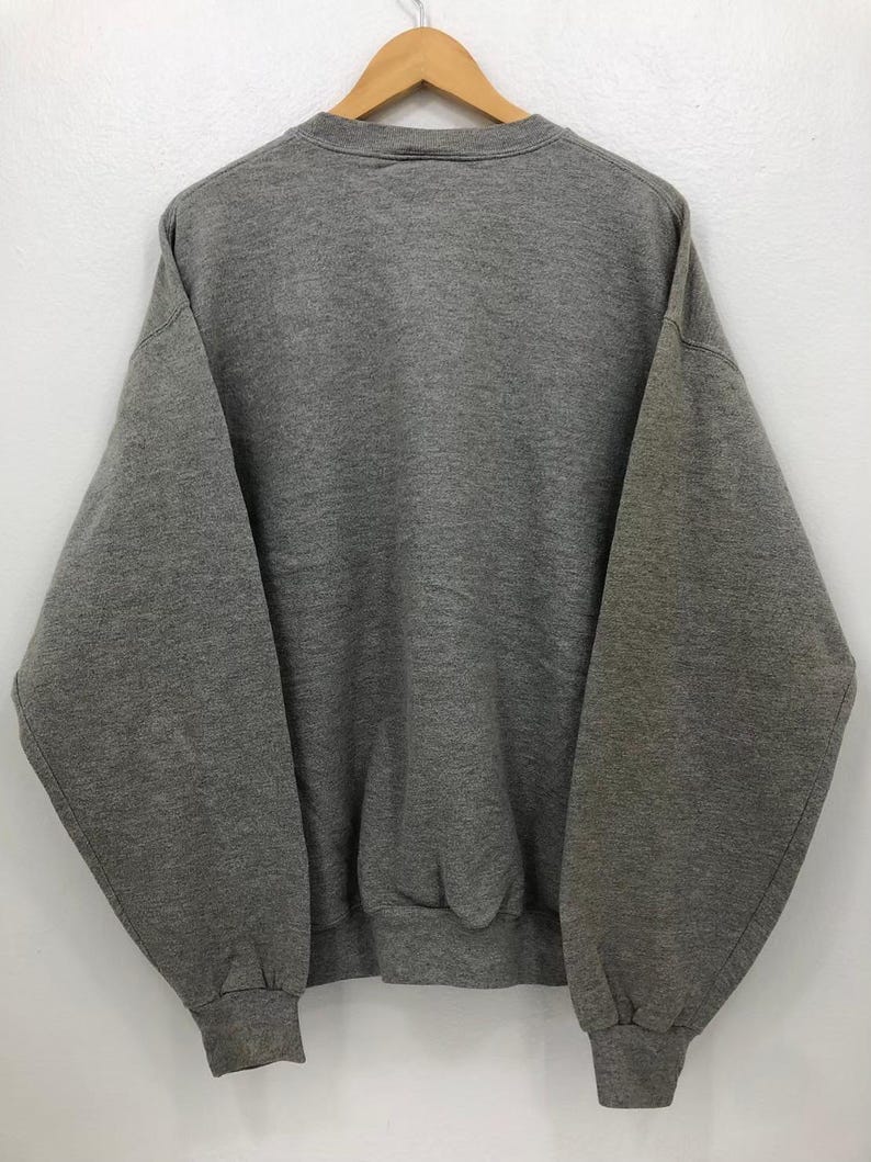 May include: A heather gray sweatshirt with a crew neck and long sleeves. The sweatshirt is hanging on a wooden hanger against a white background. The cuffs and hem are ribbed.
