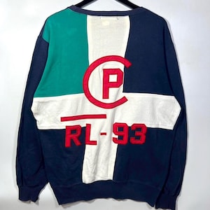 May include: A color-blocked sweatshirt with a green, white, and navy blue design. The back features a large red "C" with a "P" inside, and the text "RL-93" in red. The sweatshirt has long sleeves and a crew neck.
