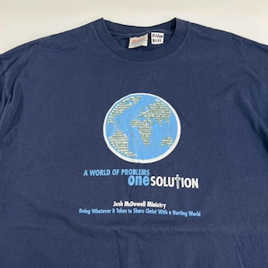 May include: Navy blue t-shirt with a graphic of a globe and the text "A WORLD OF PROBLEMS one SOLUTION". The shirt also includes the text "Josh McDowell Ministry" and "Doing Whatever It Takes to Share Christ With a Hurting World".
