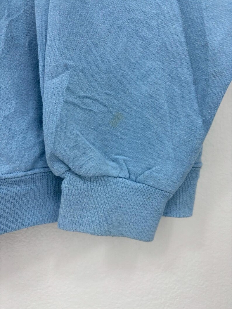 以下が含まれることがあります： リブ編みの袖口と裾が付いた、明るい青色のスウェットシャツ。生地は柔らかいニット素材のようです。袖に小さなシミがあります。